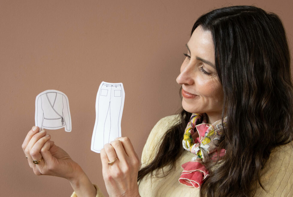 image-02: Sarai holding up cut out flats of a complex jeans project and a simple wrap sweater