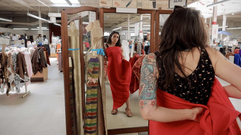 Sarai draping fabric over themselves in front of a mirror at a fabric store