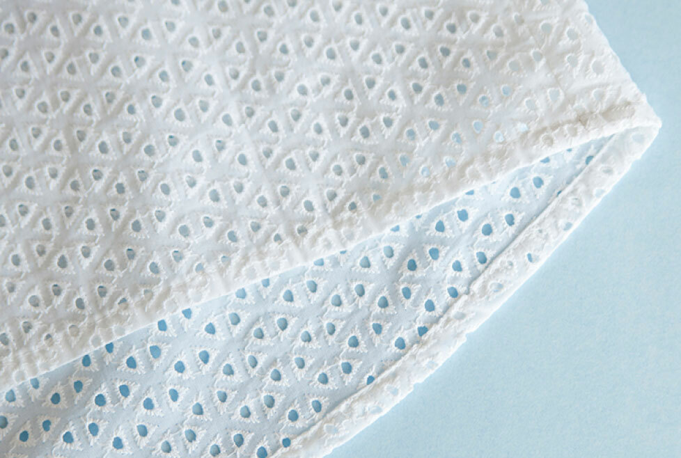 [image-05: Close-up of eyelet fabric showing the embroidered pattern and holes alongside a completed eyelet garment with scalloped edges at the hem]