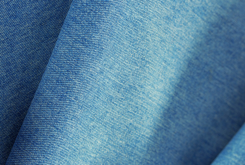 [image-06: Close-up of denim fabric showing the characteristic diagonal twill weave and demonstration of using a clapper to press a denim seam flat]