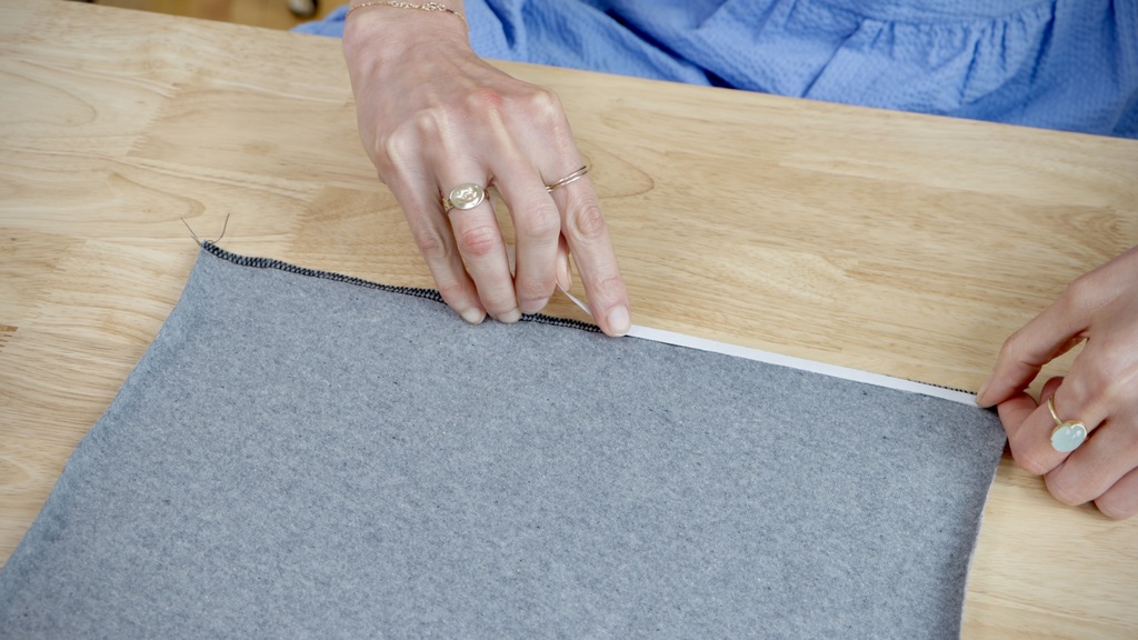 Hands applying Wonder Tape to secure a knit hem before stitching